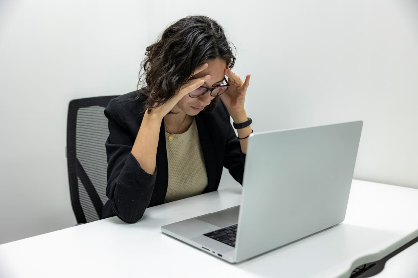 A woman at her laptop late in the day, hands pressed to her temples