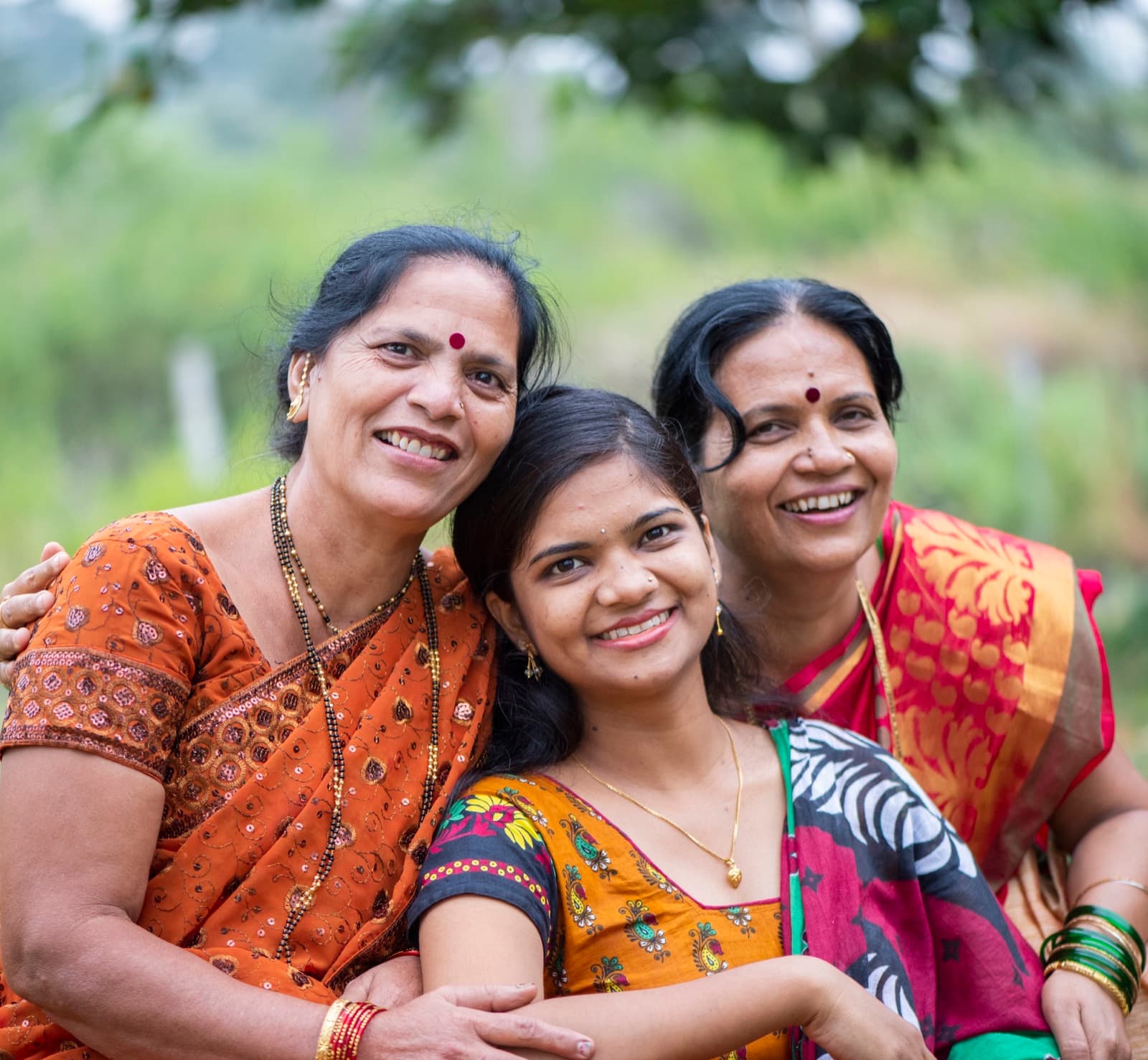 Three generations of Indian women in saris, smiling together outdoors